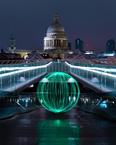 Glowing green sphere on a lit bridge with cathedral dome illuminated in background at night.