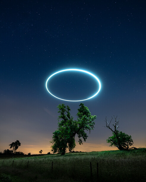 Glowing neon oval halo hovering above a solitary tree in a twilight landscape.