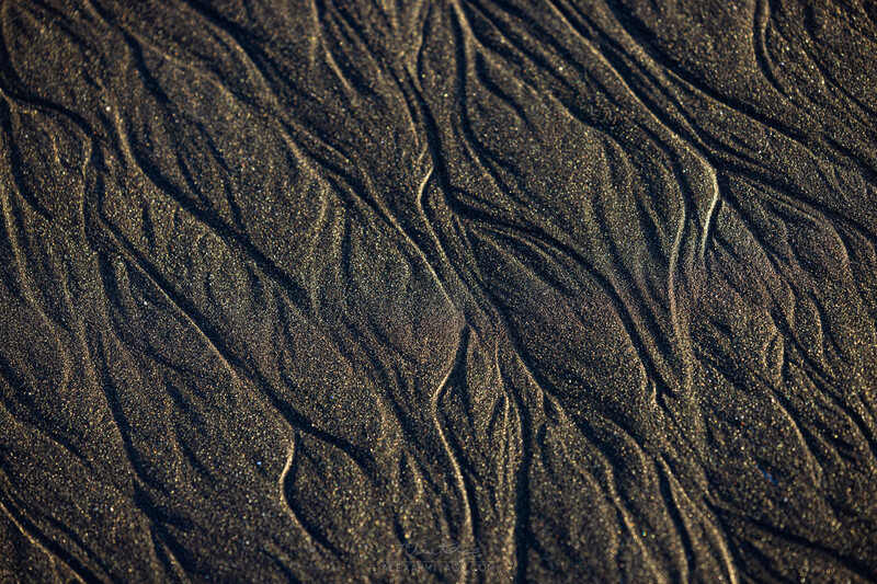 Wet sand surface with water rivulets and organic flow patterns creating natural abstract textures.