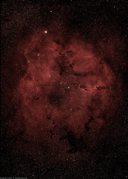 Deep red nebula cloud with dark dust lanes and scattered stars against black space.
