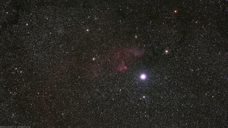 Deep-sky astrophotography showing a bright star surrounded by nebulosity and numerous fainter stars against dark space.