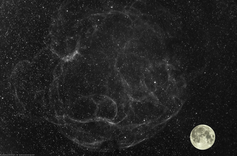 Full moon positioned next to a nebula region filled with stars against a dark night sky.