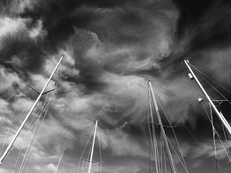 Sailboat masts silhouetted against dramatic, churning storm clouds in black and white.