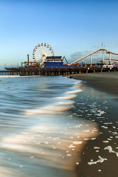 Santa Monica Pier amusement park extending into the Pacific Ocean at sunset with soft waves in foreground.