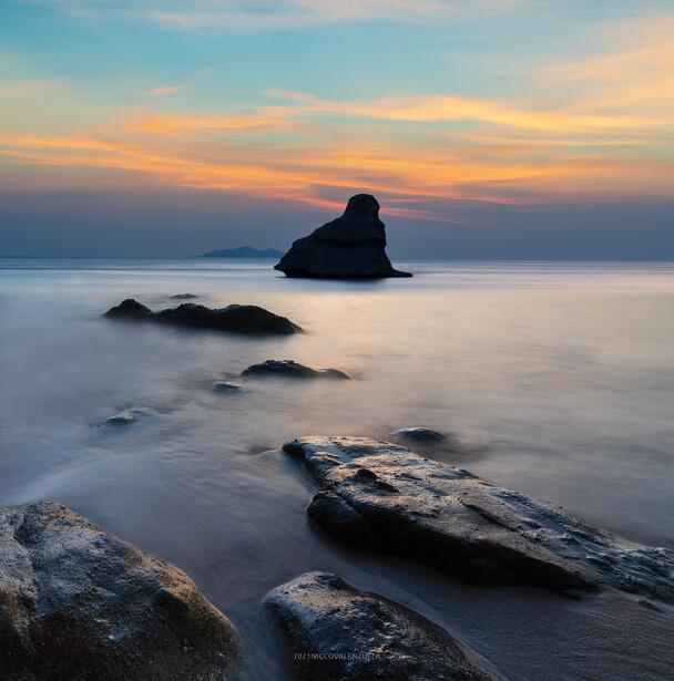 Silhouetted rock formations and sea stack during golden hour coastal sunset.