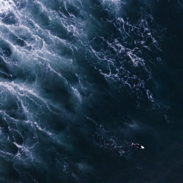 Aerial view of a small boat surrounded by churning ocean waves with white foam patterns.