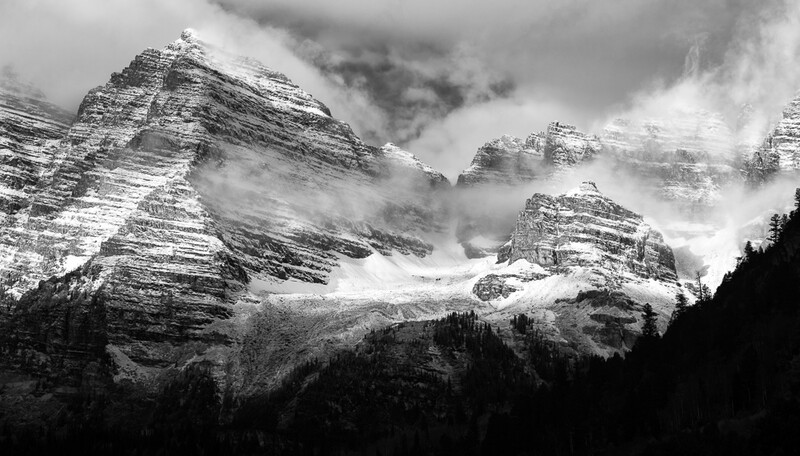 Snow-covered mountain peaks with layered geological formations, partially obscured by clouds and mist.