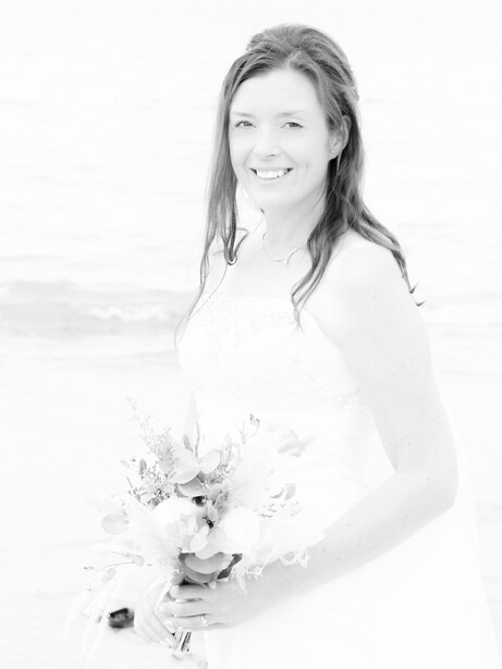 Bride in white dress holding bouquet on beach, black and white portrait.