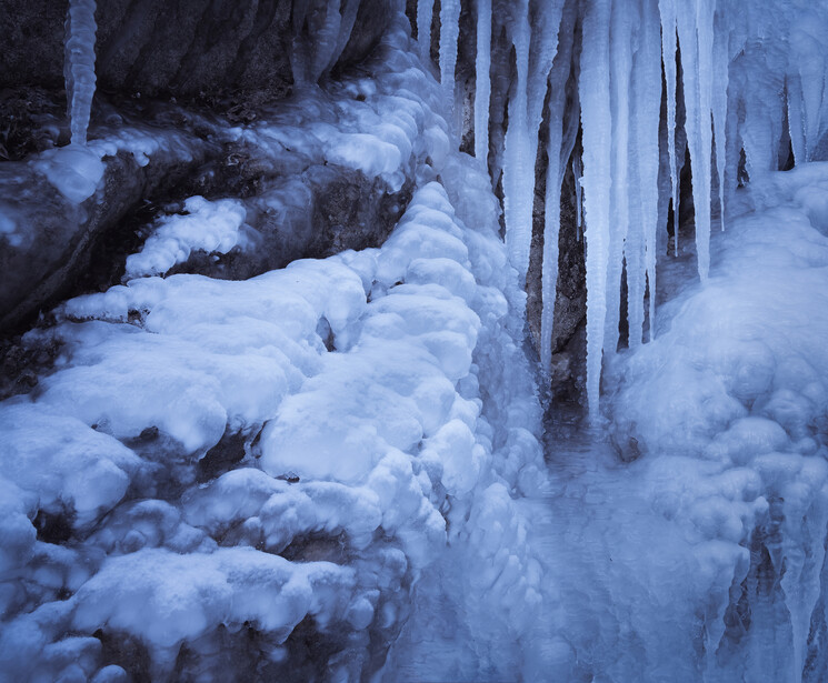 Frozen waterfall with cascading ice formations and icicles hanging from rocky cliffs.