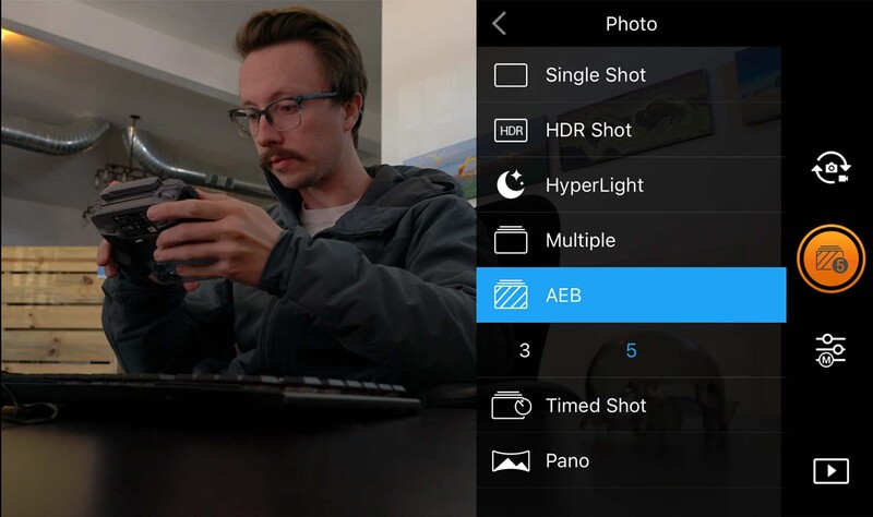 Photographer holding a camera while viewing smartphone screen displaying various photo mode options.