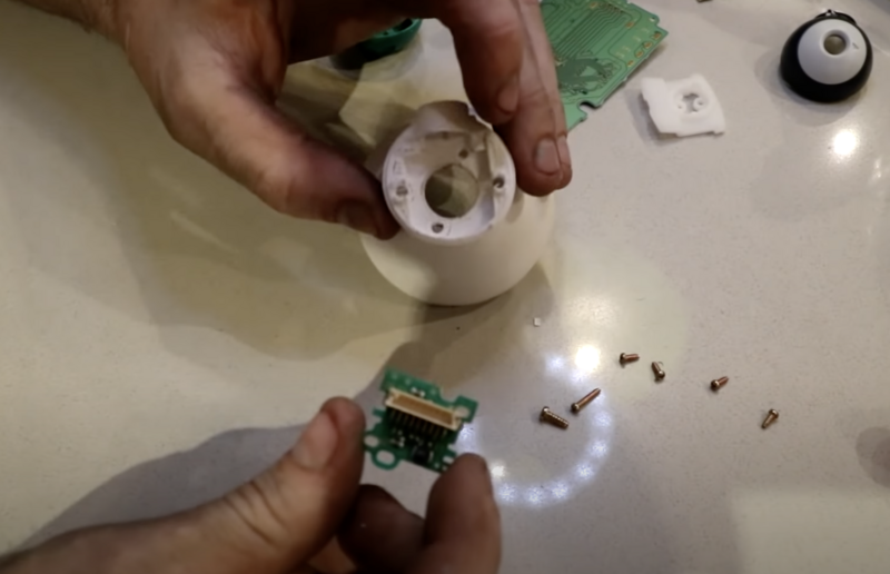 Hands disassembling an electronic device, exposing circuit board components and internal wiring.