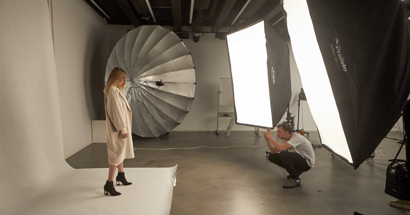 Professional studio portrait setup with model and photographer positioning reflector and softbox lighting.
