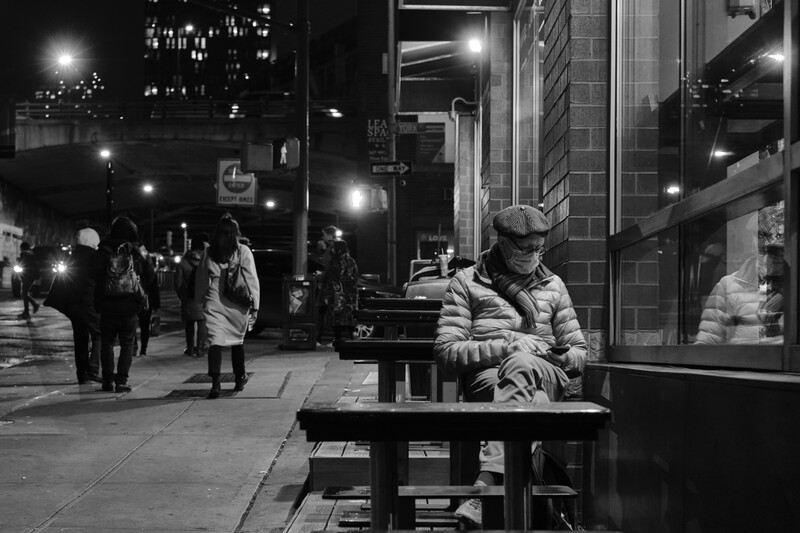 Street musician playing keyboard at night on an urban sidewalk with pedestrians and illuminated storefronts.