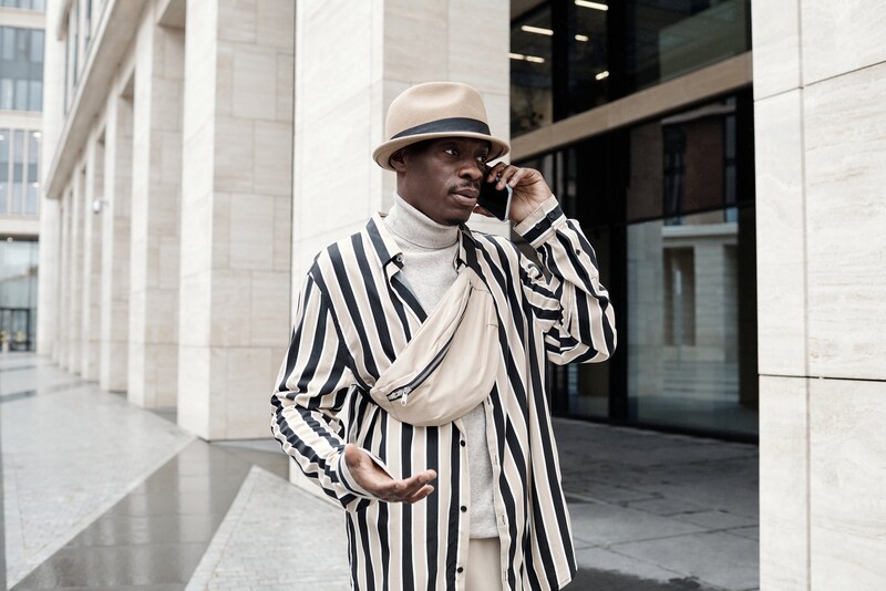 Man in striped blazer and Panama hat on phone in modern urban plaza.