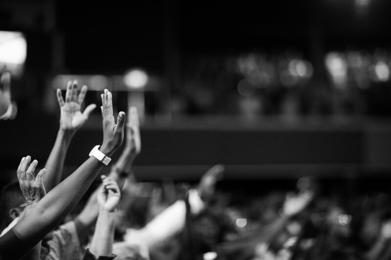 Raised hands of a crowd at an event, captured in black and white with selective focus on the foreground.