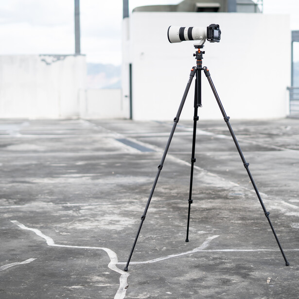 Telephoto lens mounted on tripod on a rooftop with cityscape in background.