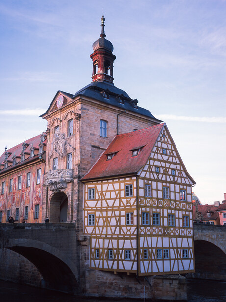 Half-timbered building with red roof and bell tower reflected in canal water below.