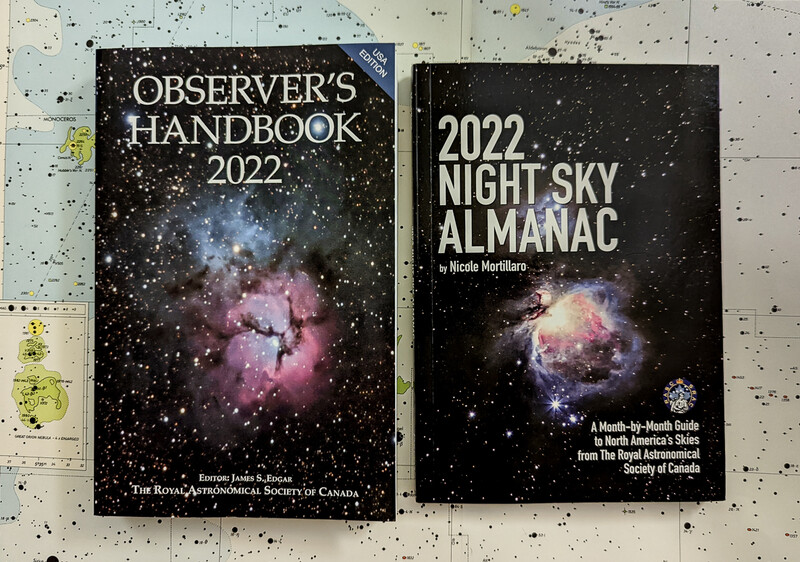 Two astronomy guidebooks displayed on a star chart: Observer's Handbook 2022 and 2022 Night Sky Almanac.
