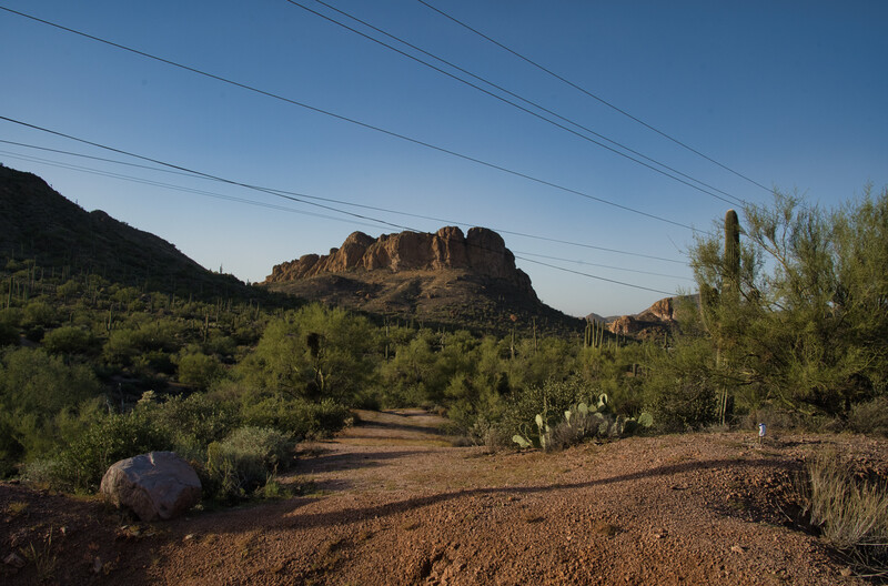 Desert landscape with distinctive layered rock formation rising above sparse vegetation and dirt road.