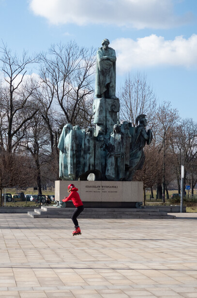 Runner in red jacket jogging past a large green patina statue in an urban plaza with bare trees.