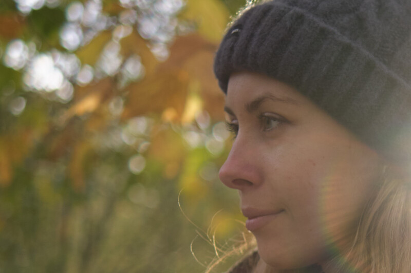 Woman in profile wearing a beanie, backlit by golden autumn foliage.
