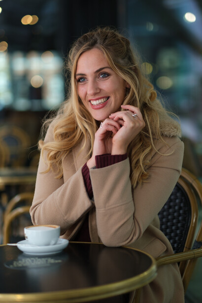Woman with blonde wavy hair smiling at camera in an evening café setting.