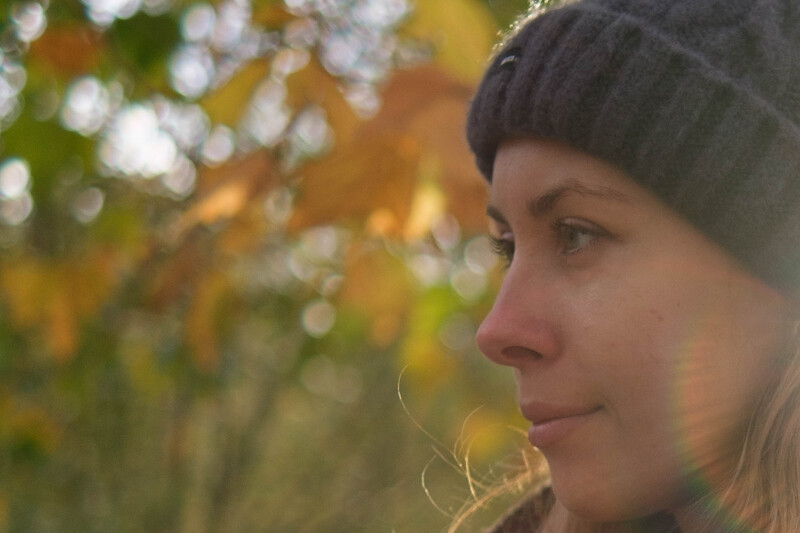 Woman in profile wearing a dark beanie, backlit by golden autumn foliage.