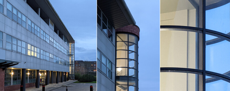Modern institutional building facade with illuminated grid windows at dusk, featuring geometric glass and metal architectural details.
