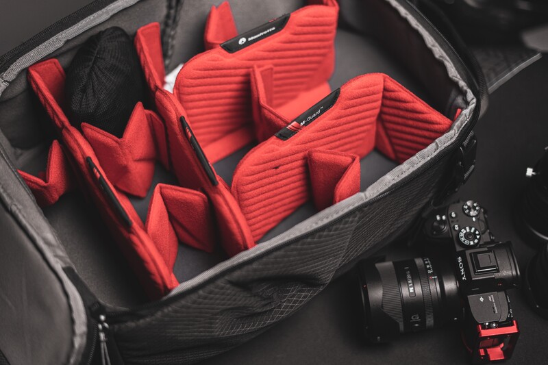 Camera gear organized in a protective case with red padded dividers and a mirrorless camera body with lens nearby.