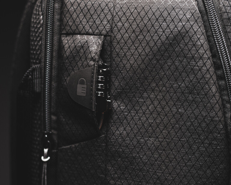 Camera with combination lock visible through mesh pocket of camera bag.