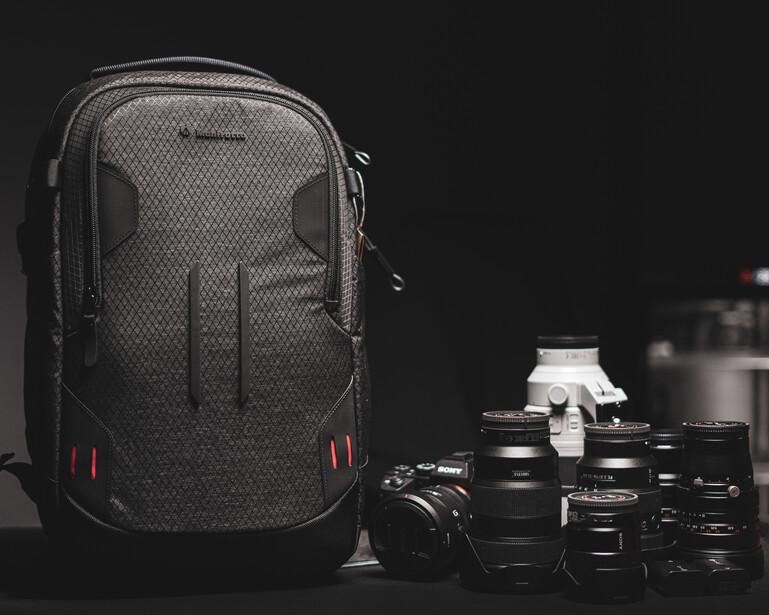 Professional camera backpack displayed with camera body and multiple lenses against dark background.