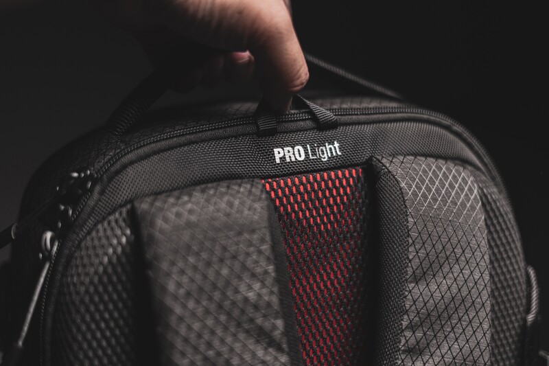 Hand holding open a camera bag with mesh compartments and red divider panels labeled PRO Light.