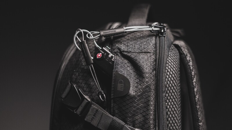 Black camera backpack photographed against dark background with dramatic side lighting highlighting texture and hardware.