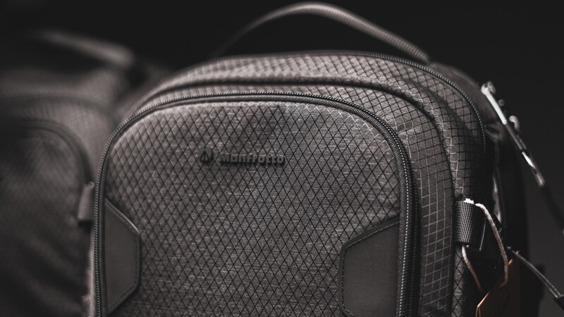 Close-up of a gray camera backpack with diamond quilted fabric and padded compartments against a dark background.