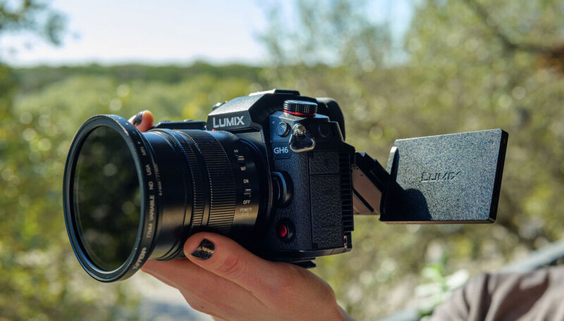 Panasonic Lumix mirrorless camera with wide-angle lens held in hand outdoors, articulating screen extended.