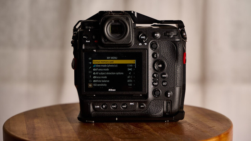 Professional mirrorless camera displaying menu settings on rear LCD screen, positioned on wooden surface.