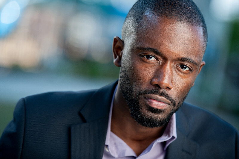 Professional headshot of a man with a beard wearing a dark blazer and light pink shirt.