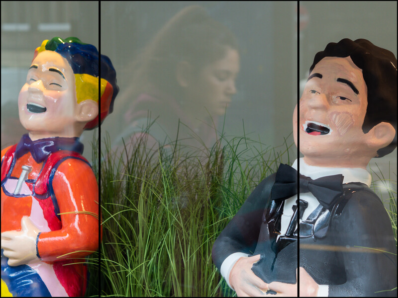 Two cartoon character figures displayed in window reflections with natural foliage backdrop.
