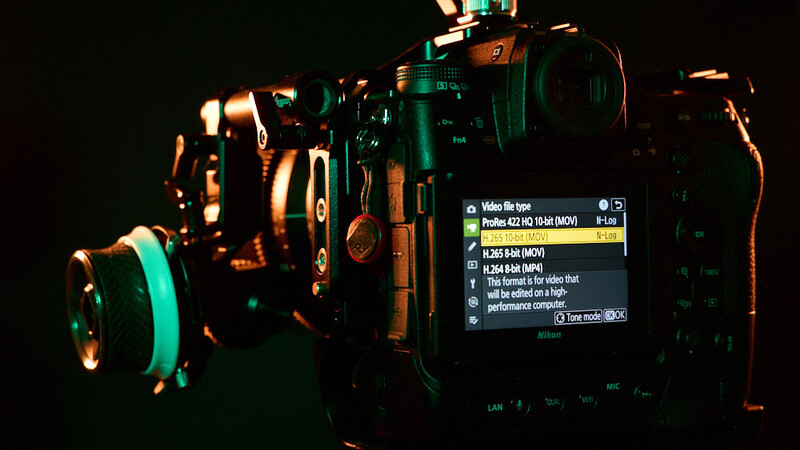Professional cinema camera with mounted lens illuminated by warm and cool gel lighting against a dark background.