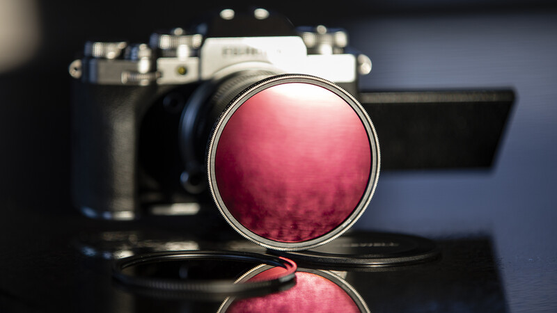 Red filter for camera lens positioned in front of vintage rangefinder camera and film camera body.