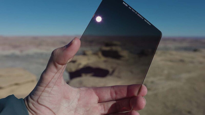 Hand holding smartphone displaying moon and desert landscape in reflection against arid terrain background.