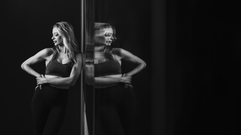 Woman in black athletic wear posing with hands on hips next to a mirror, creating a symmetrical reflection.