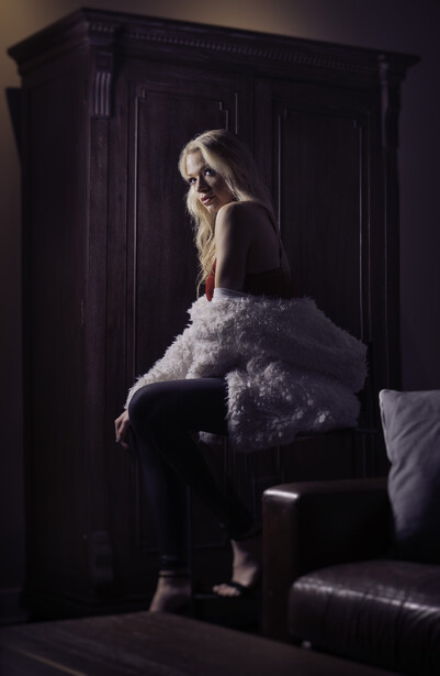 Woman in white tulle skirt sitting on dark furniture against black wardrobe backdrop.