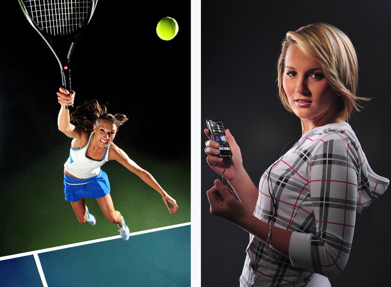 Female tennis player serving on an indoor court with dramatic backlighting against dark background.