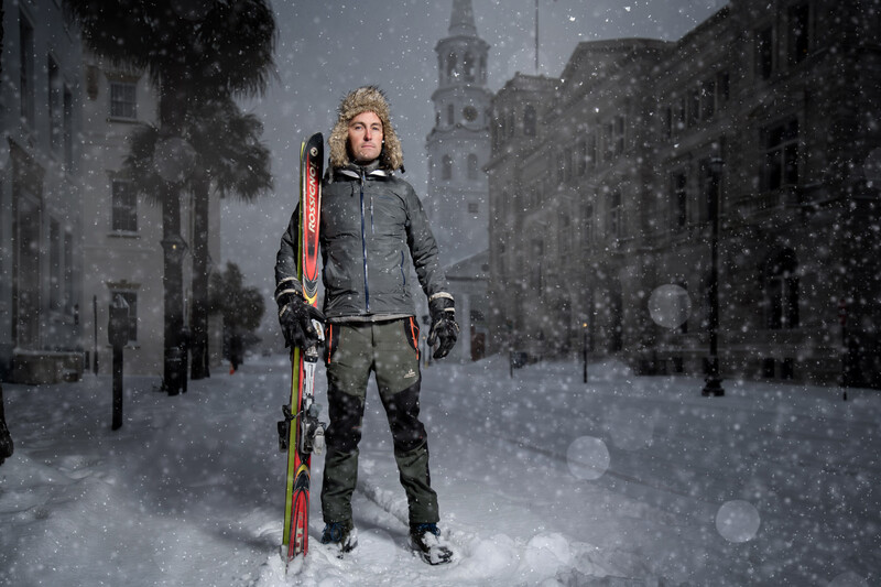 Woman holding skis standing in heavy snowfall on a snowy urban street with historic buildings.