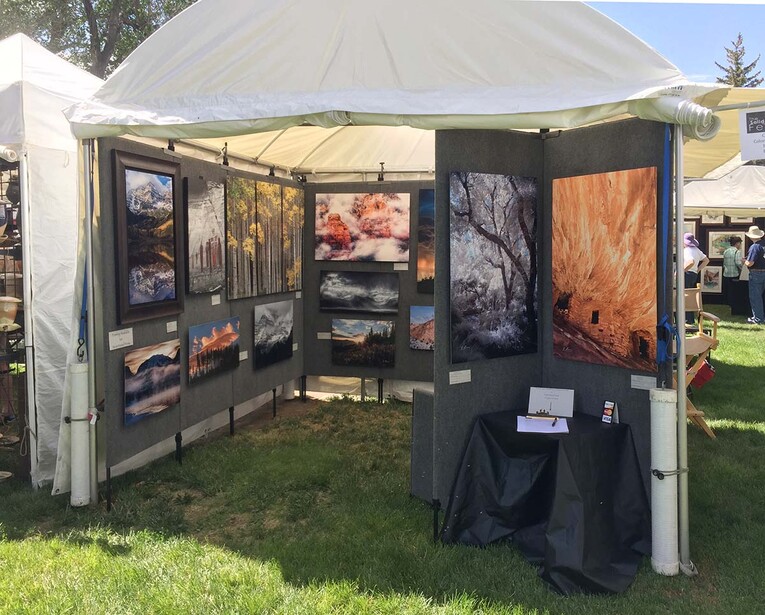 Photography exhibition booth under a white tent displaying large-format landscape and nature prints on black panels.