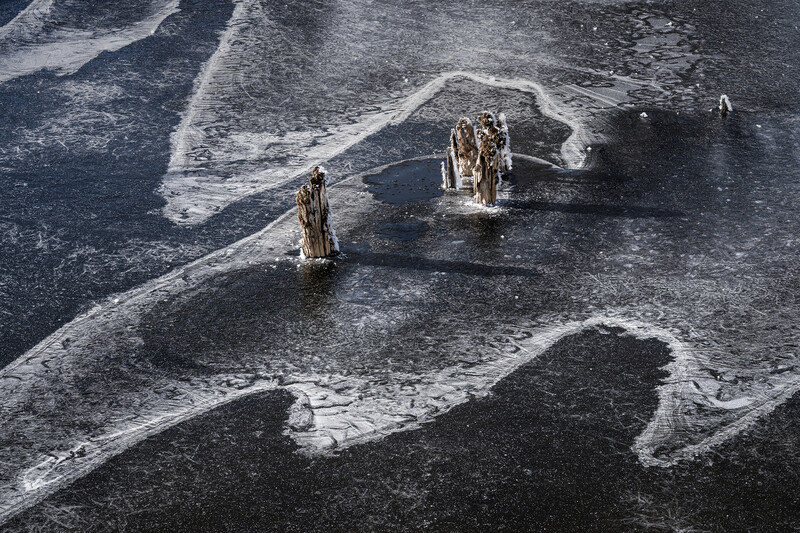 Aerial view of wooden pilings emerging from rippled tidal flats and shallow water.