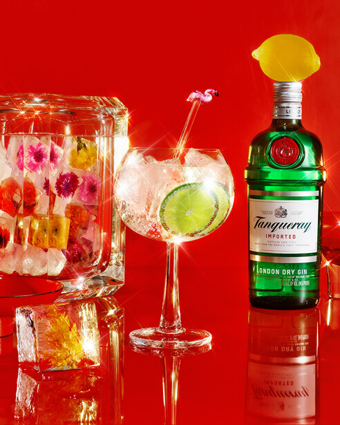 Still life arrangement of cocktails and a bottle against a bright red background.