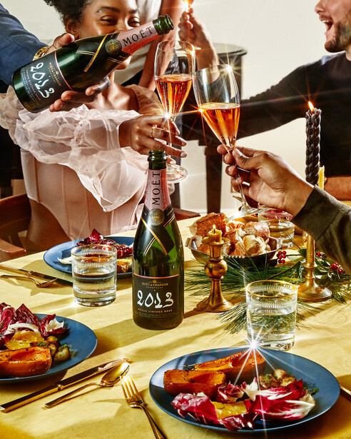 Champagne being poured into glasses at an outdoor table setting with plated food and wine bottles.