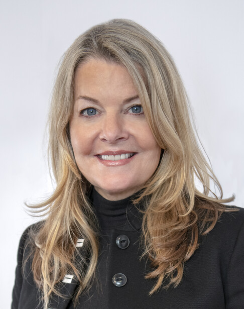 Professional headshot of a woman with shoulder-length blonde hair wearing a black blazer against a white background.
